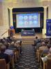 a woman at a podium in front of a screen highlighting all of the Distinguished Alumni Award winners.