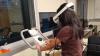 A woman on an exercise machine wearing a VR headset in an office or lab.