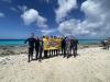 group of scuba trip attendees holding georgia tech flag on beach