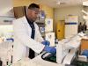 A man in a lab coat wearing safety goggles and gloves puts samples into a machine in a scientific lab