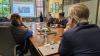 Several people seated around a conference table listen to a presentation with a presentation slide that reads, "Technology creates possibilities. The liberal arts turns those possibilities into impact."