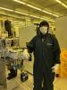 Dean Sutter stands beside semiconductor fabrication equipment in a Georgia Tech cleanroom while wearing full cleanroom protective attire and a face mask.