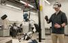 Person wearing a virtual reality headset controlling a humanoid robot equipped with tools in a laboratory setting.