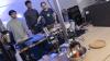 Three men use their phones to control a robot arm