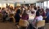 A full house of students, faculty, and staff gathered at tables. 