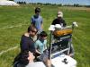 Five members of the RoboJackets stand around their robot on a grass field and analyze the robot's software.