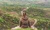 Woman sitting with her back to the camera on top of a rock overlooking treetops.