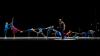 Against a black background, a group of dancers are arranged in a line, arms and legs reaching to each other.