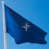 A blue flag with the NATO logo on it flying in a clear blue sky.