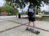 Photo of student riding a e-skateboard with a helmet on on campus.