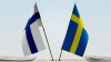 Finland's and Sweden's flags sit on top of a desk.