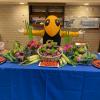 Buzz behind a table with fruits and vegetables.