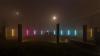 foggy, dark nighttime photo with multiple pillars, glowing in different colors, arranged in a semi circle