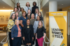 group of women standing on staircase smiling next to a banner that says Leading Women@Tech