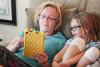 Mom and daughter look at a tablet together sitting on the couch.